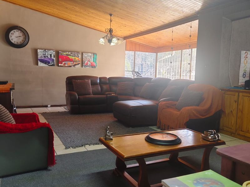 Spacious living room featuring a distinctive timber-clad raked ceiling, large corner windows for natural light, and tiled flooring.