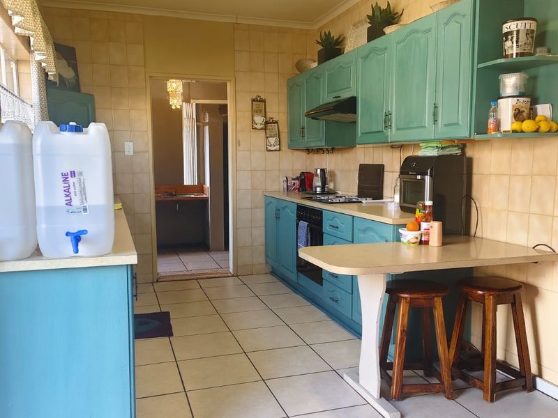 A functional kitchen featuring teal cabinetry, tiled splashbacks, and tiled flooring, offering a dated aesthetic with potential for modern renovation.