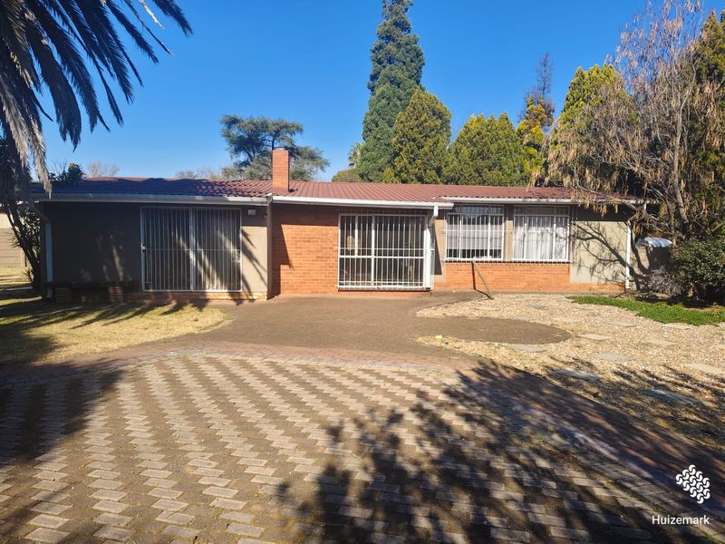 Rear view of a single-story brick house featuring a metal roof, security bars on windows and doors, and a paved patio area.