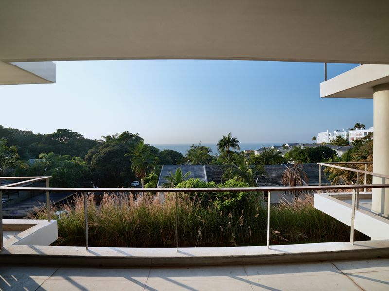 Spacious covered balcony featuring a modern metal railing and tiled flooring, offering expansive views of the surrounding landscape and ocean.