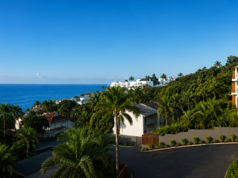 Elevated coastal view overlooking the ocean, lush tropical landscape, and the apartment complex exterior with timber privacy screens and balconies.