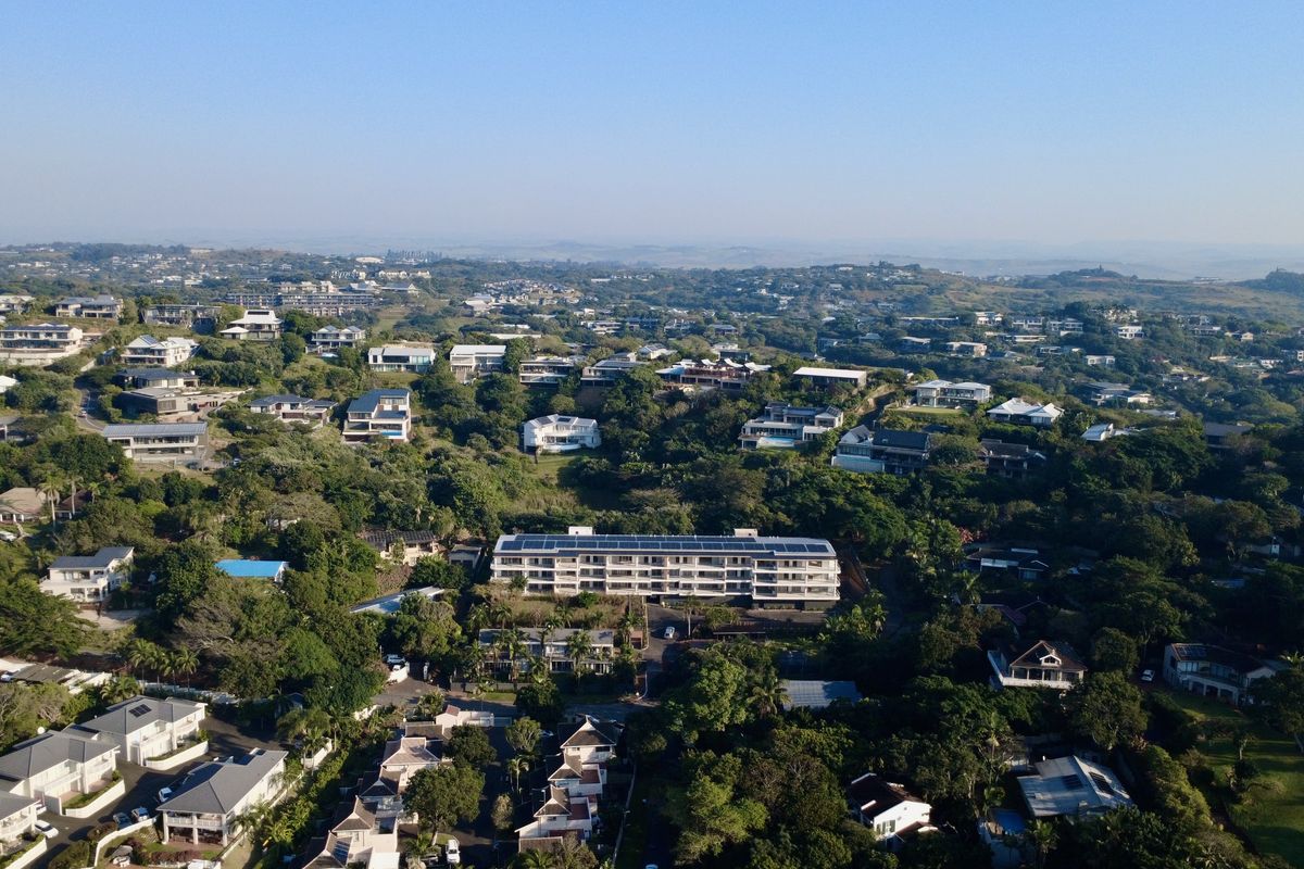 An aerial view of the residential estate showcasing the apartment building with rooftop solar panels surrounded by lush greenery and neighboring properties.