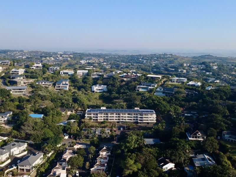 An aerial view of the residential estate showcasing the apartment building with rooftop solar panels surrounded by lush greenery and neighboring properties.