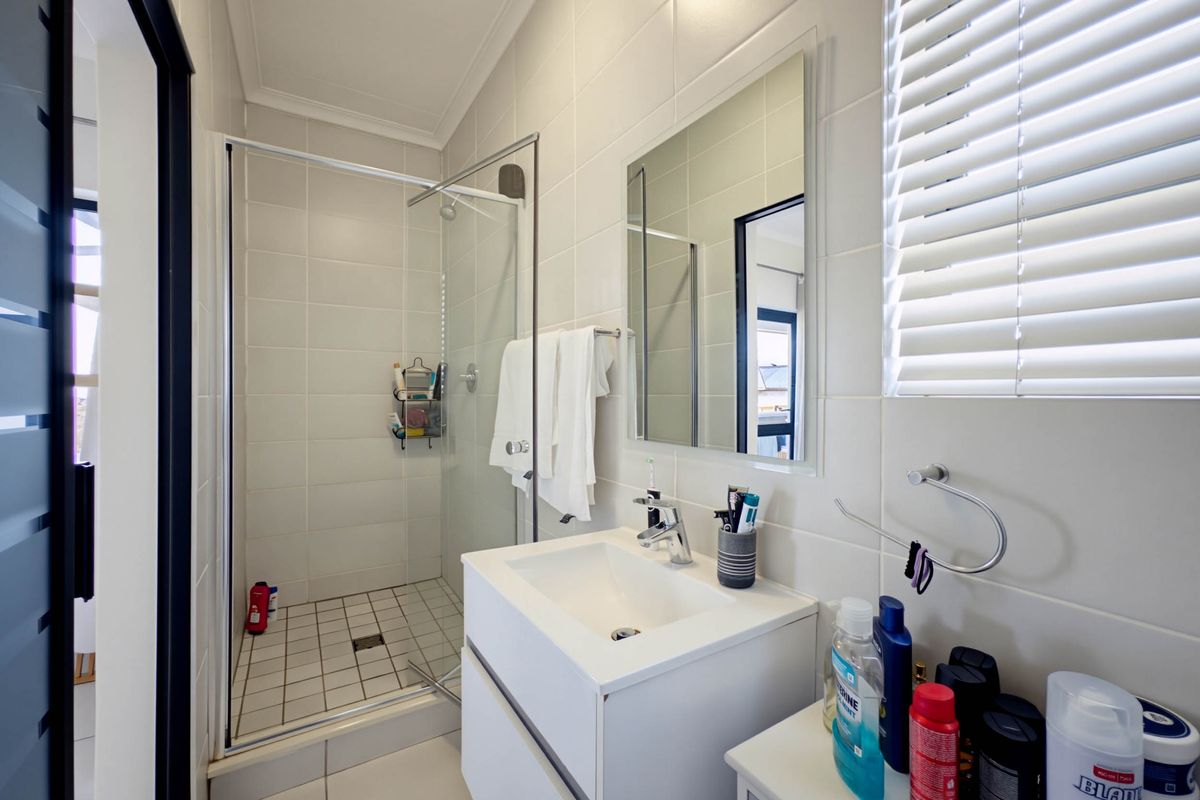 A clean, modern bathroom featuring a glass-enclosed shower, wall-mounted vanity with basin, and neutral tiled finishes throughout.