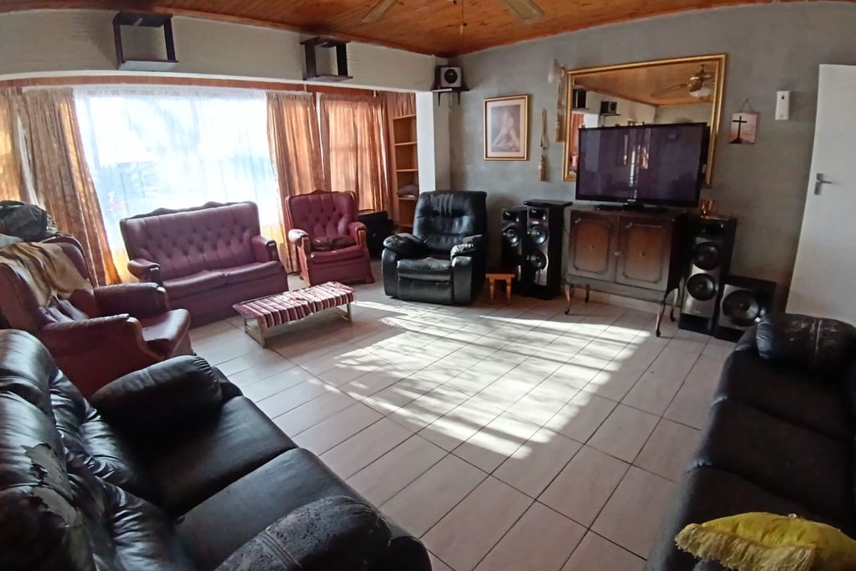 Spacious living room featuring tiled flooring, a timber-clad ceiling with a ceiling fan, and large windows allowing for natural light.