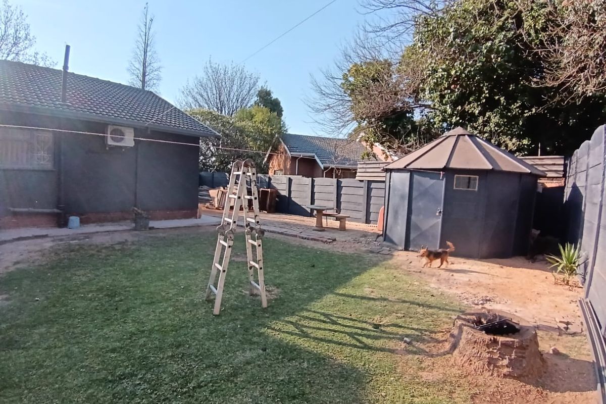Rear garden area featuring a lawn, precast boundary walling, and a detached outbuilding structure.