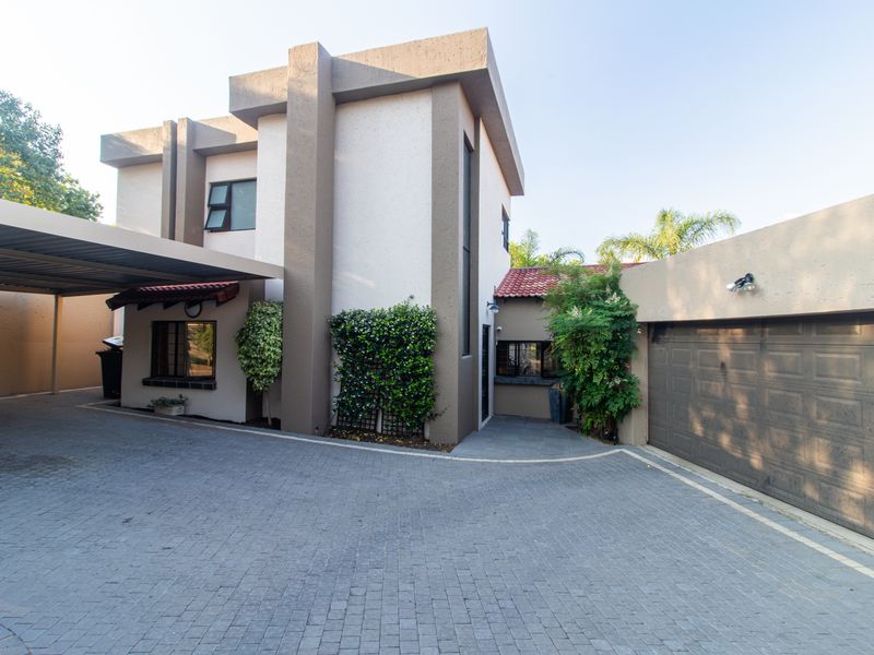 Front elevation of a modern cluster home featuring a paved driveway, covered carport, and a secure garage entrance.
