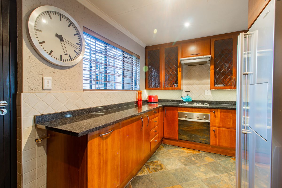 A functional kitchen featuring warm wooden cabinetry, granite countertops, a built-in oven with gas hob, and durable slate flooring.
