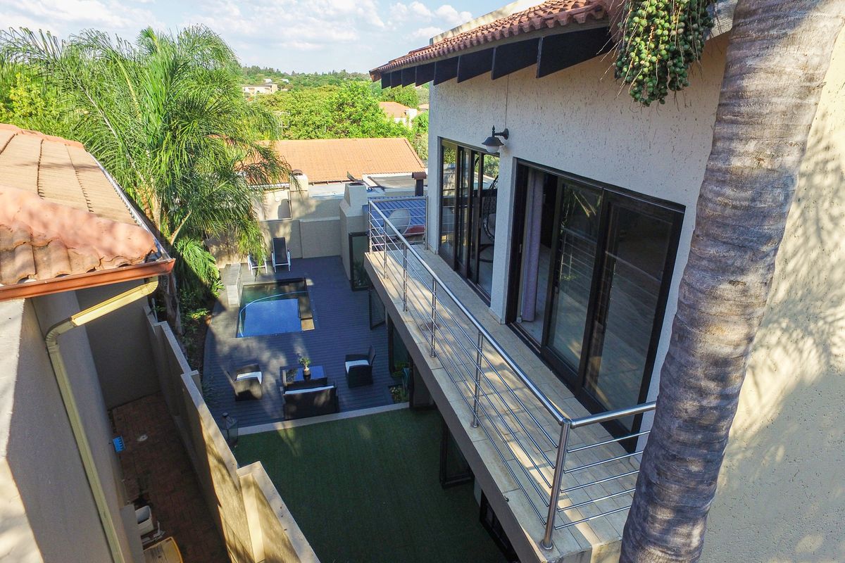 Elevated view of the rear exterior featuring a balcony with stainless steel balustrades, a swimming pool, decking, and an artificial lawn area.