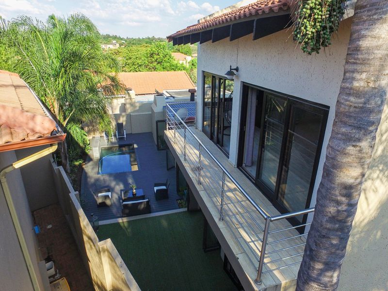 Elevated view of the rear exterior featuring a balcony with stainless steel balustrades, a swimming pool, decking, and an artificial lawn area.
