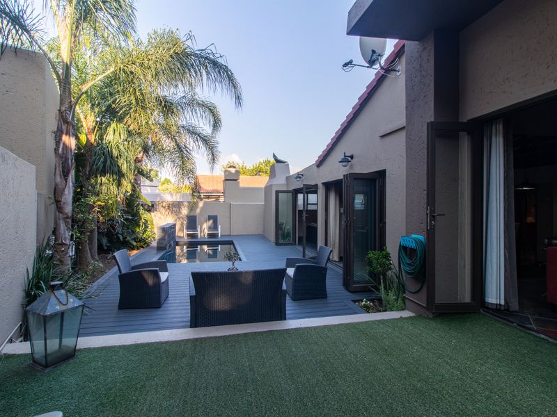 A private rear courtyard featuring a modern swimming pool, composite decking, and artificial lawn, seamlessly connected to the interior living space via bi-fold doors.