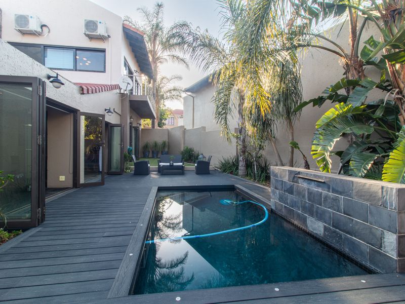 Private outdoor pool area featuring dark timber decking, a stone water feature wall, and seamless access to the interior via large bi-fold doors.