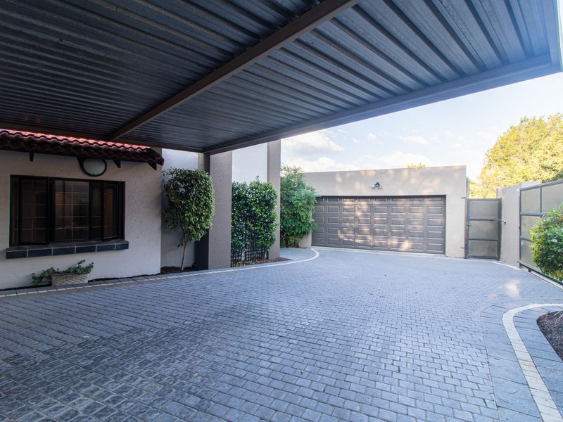 A well-maintained front exterior featuring a paved driveway, a covered carport, and a secure garage entrance.