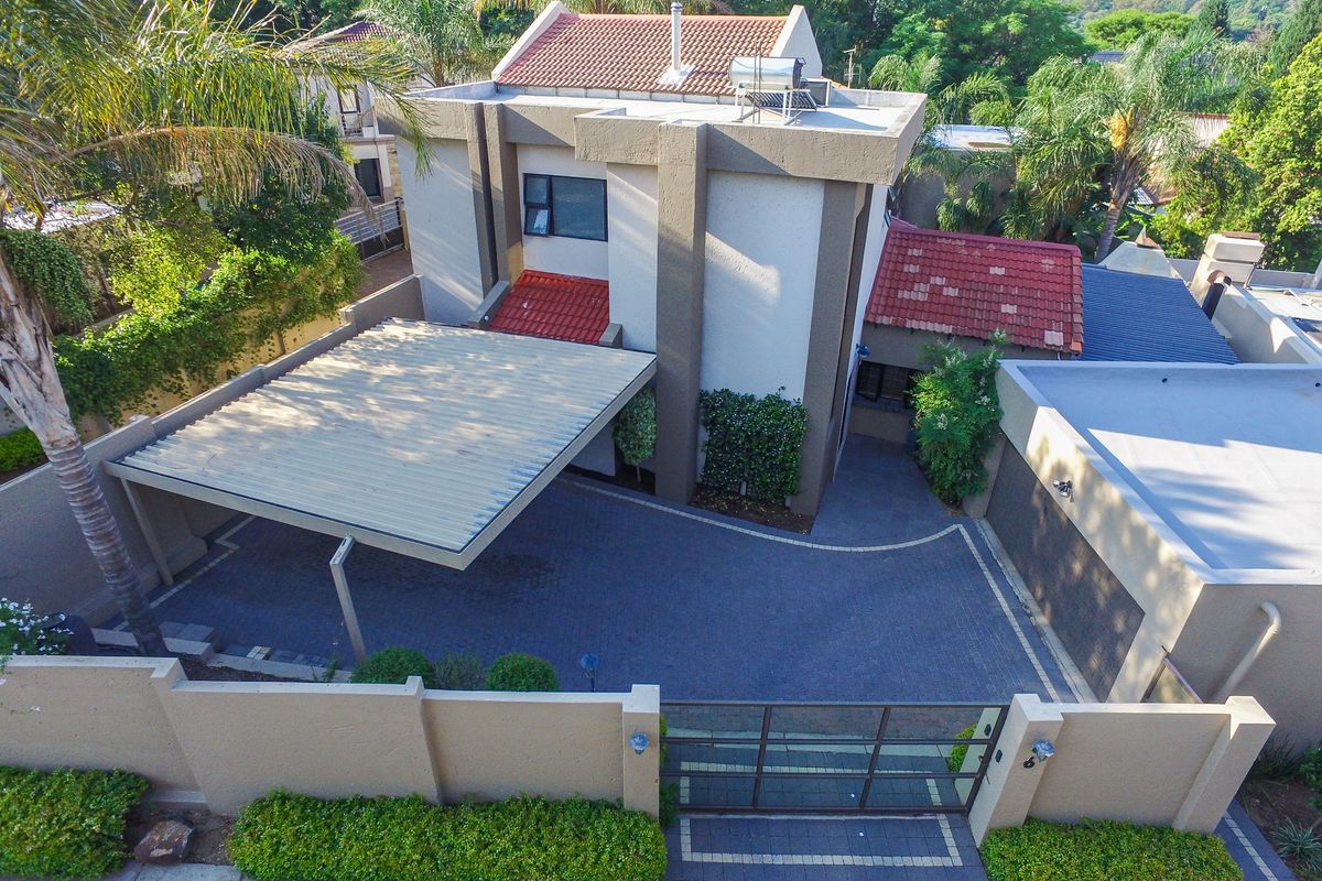 Aerial view of a cluster home featuring a paved driveway, covered carport, garage, and secure boundary wall with gated entrance.