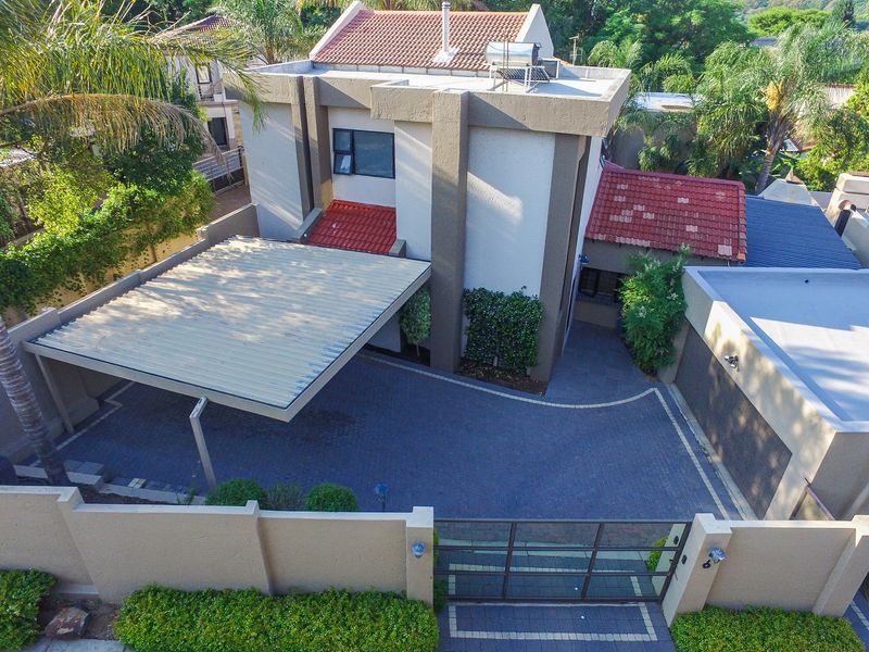 Aerial view of a cluster home featuring a paved driveway, covered carport, garage, and secure boundary wall with gated entrance.
