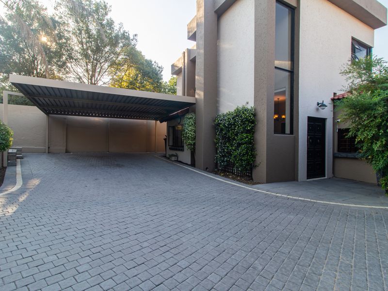 A modern double-storey cluster home featuring a paved driveway, a spacious carport, and a well-maintained exterior facade with vertical window detailing.