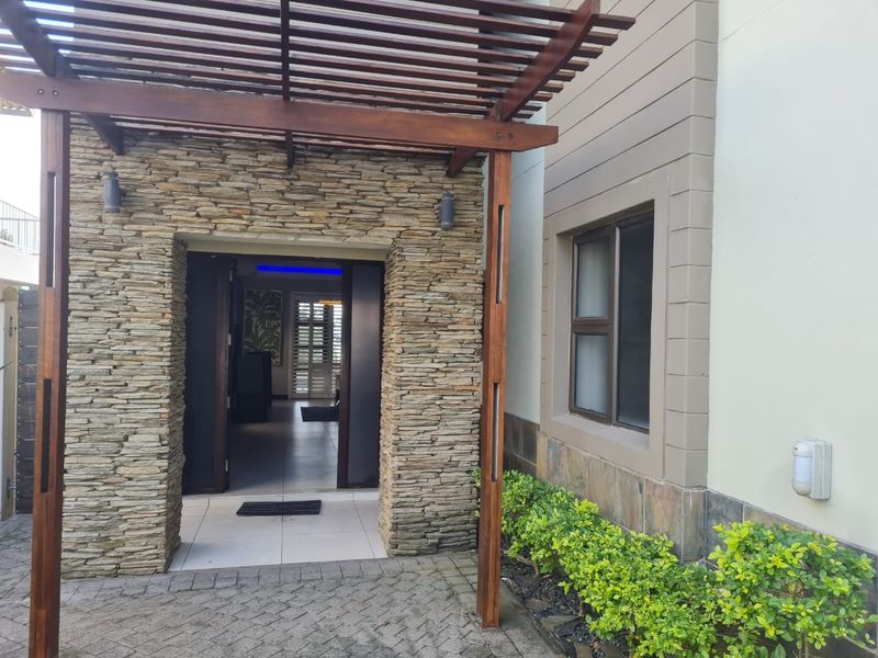 Inviting entrance featuring a timber pergola, natural stone cladding, and a paved walkway leading to the main doorway.