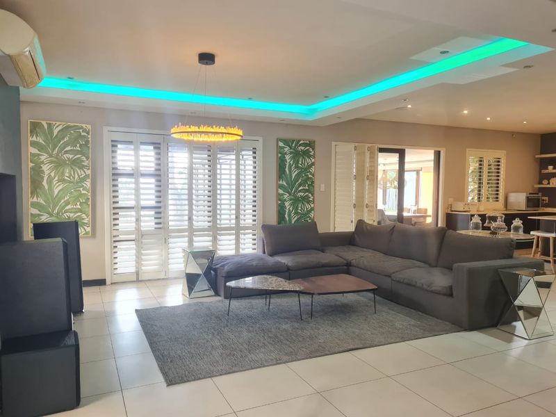 Spacious open-plan living area featuring modern recessed ceiling lighting, tiled floors, and plantation shutters, seamlessly connecting to the kitchen and outdoor spaces.