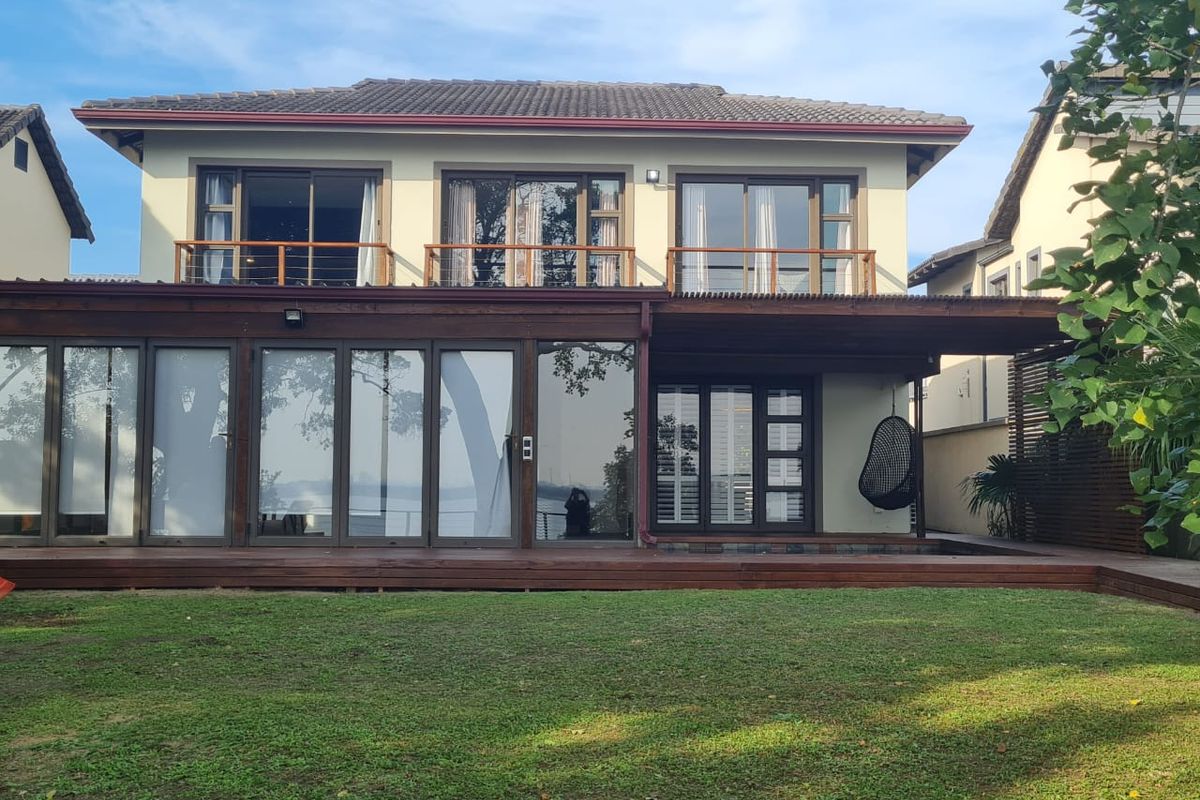 Rear view of a two-story house featuring extensive timber decking, a covered patio area, and multiple sliding glass doors leading to upper-level balconies.