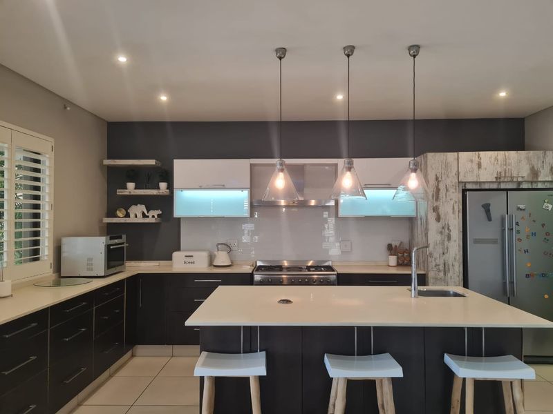 Modern kitchen featuring a central island with stone countertops, gas stove, extractor fan, sleek cabinetry, and stylish pendant lighting.