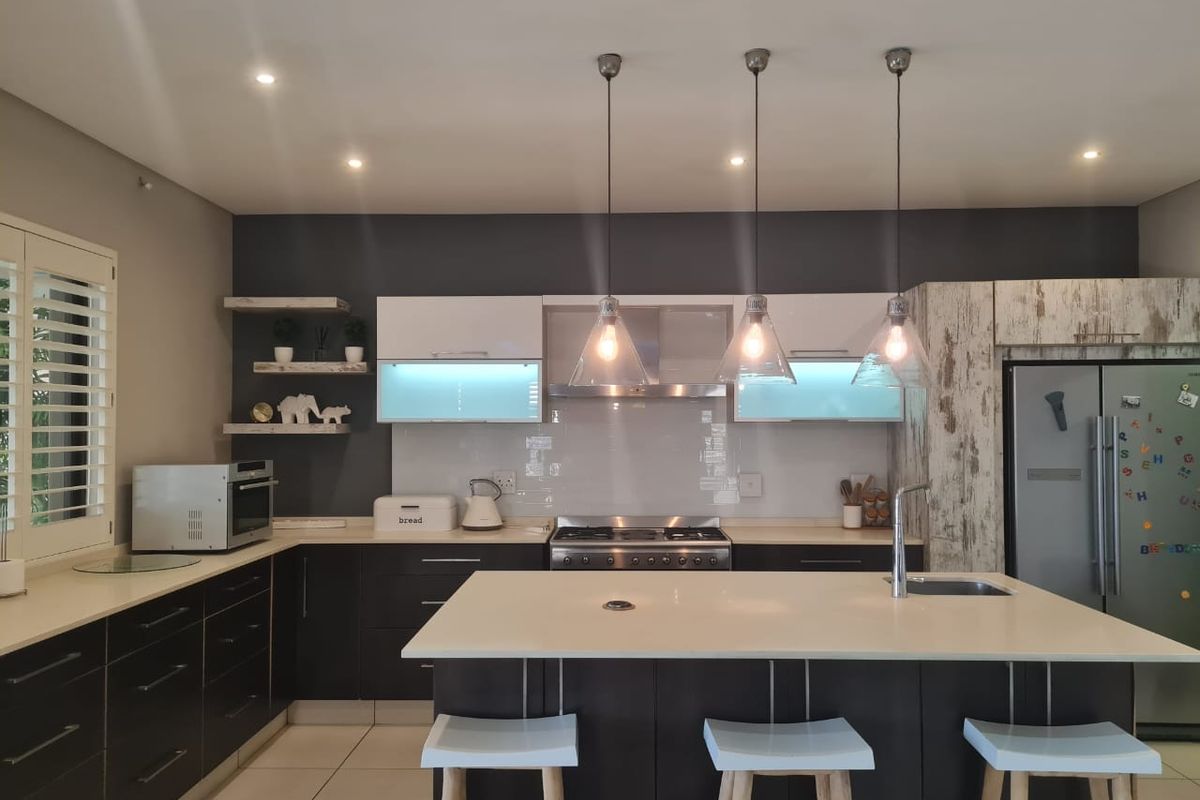 Modern kitchen featuring a central island with stone countertops, gas stove, extractor fan, sleek cabinetry, and stylish pendant lighting.