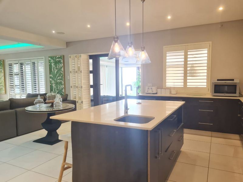 Modern open-plan kitchen featuring a central island with stone countertops, sleek cabinetry, and stylish pendant lighting, seamlessly flowing into the living area.