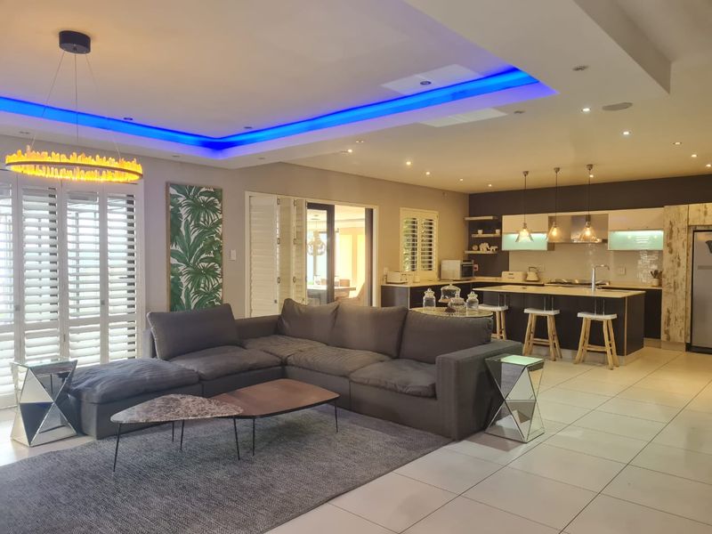 Spacious open-plan living area featuring a modern kitchen with island, recessed ceiling lighting, and tiled floors, seamlessly connecting to the lounge space.