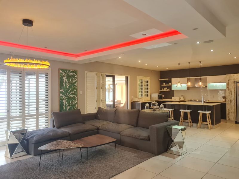 Spacious open-plan living and kitchen area featuring modern cabinetry, a central island, recessed ceiling lighting with LED accents, and large plantation shutters.