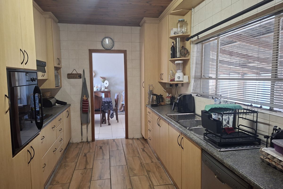 A functional galley-style kitchen featuring light wood cabinetry, tiled backsplash, timber ceiling, and integrated oven, offering a practical layout for daily meal preparation.