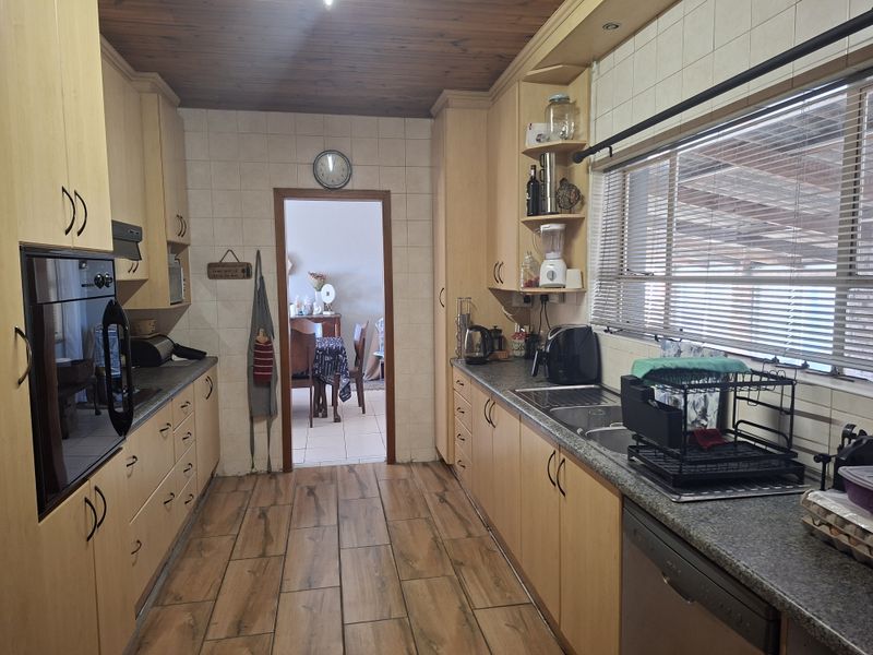 A functional galley-style kitchen featuring light wood cabinetry, tiled backsplash, timber ceiling, and integrated oven, offering a practical layout for daily meal preparation.