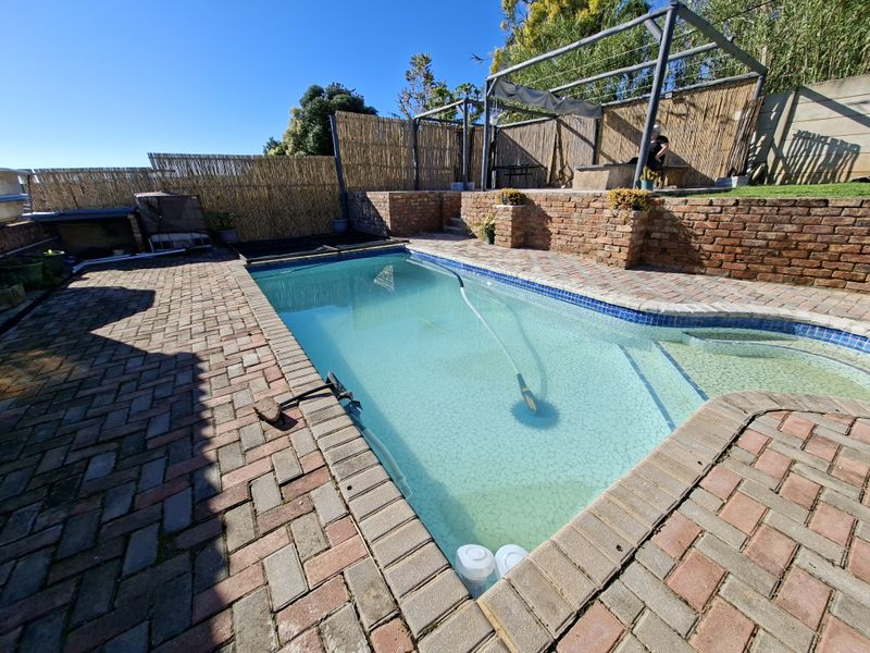 Outdoor pool area featuring a swimming pool, brick paved surround, raised brick retaining walls, and a pergola structure with bamboo privacy fencing.