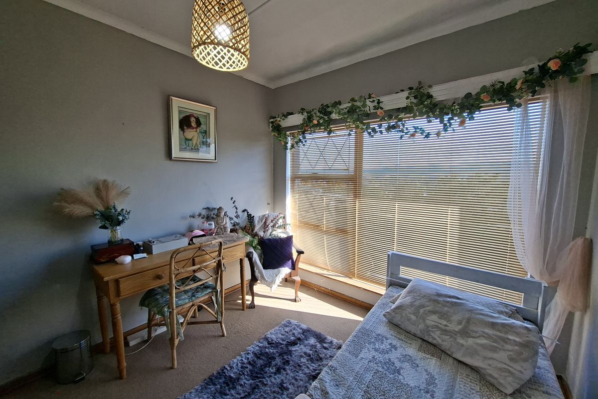 A cozy bedroom featuring a large window with venetian blinds, neutral wall tones, and carpeted flooring.
