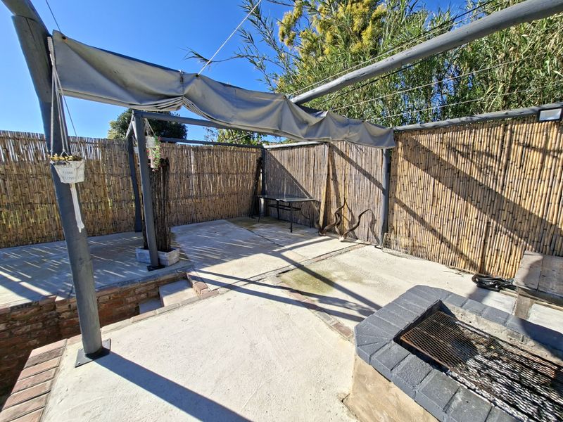 Outdoor patio area featuring a built-in braai, concrete flooring, and retractable awning, enclosed by bamboo fencing for privacy.