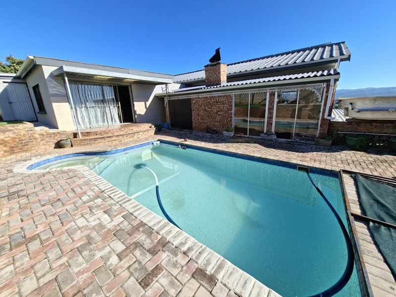Outdoor pool area featuring a swimming pool, brick paving, and a covered patio area attached to the rear of the house.
