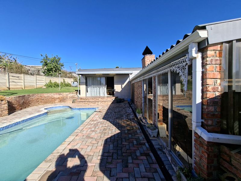 Rear exterior view featuring a swimming pool, brick paved patio area, and direct access to the home through sliding glass doors.