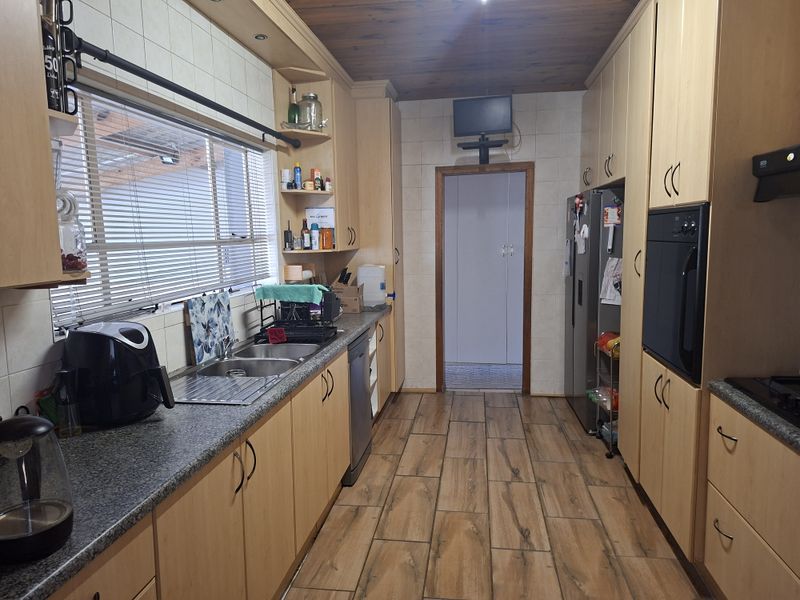 A functional kitchen featuring light wood cabinetry, granite-look laminate countertops, a double stainless steel sink, built-in oven, and wood-paneled ceiling.