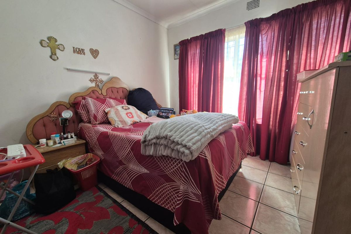 A functional bedroom featuring tiled flooring and window security bars, providing a standard living space with natural light.