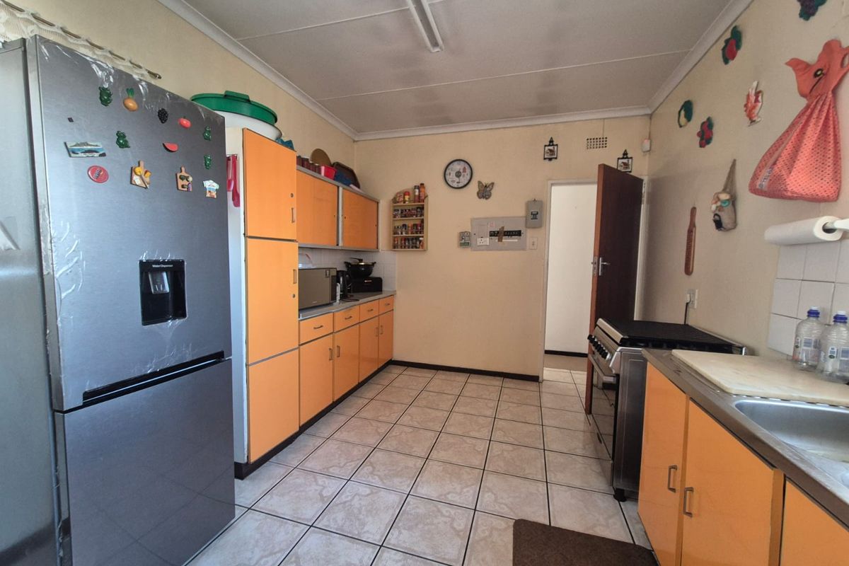 A functional kitchen featuring dated orange cabinetry, tiled flooring, and a stainless steel sink, offering potential for a modern renovation.