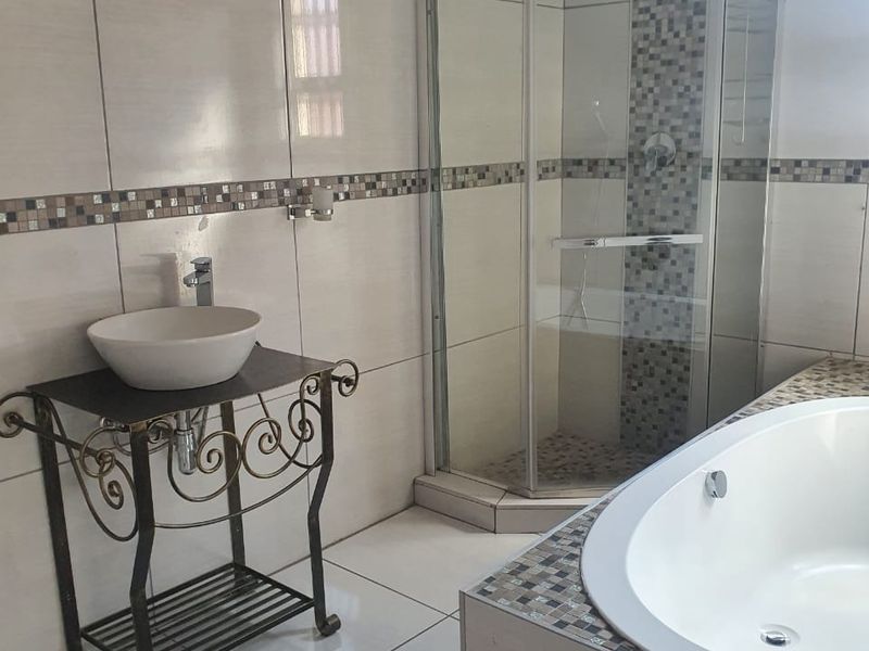 A bathroom featuring a corner shower enclosure, a built-in bathtub with mosaic tile detailing, and neutral ceramic wall and floor tiles.
