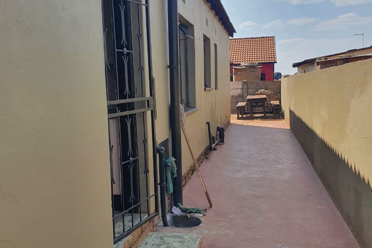 A narrow side passage of the house featuring a painted concrete pathway, security gate, and boundary wall.