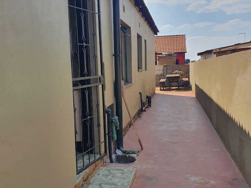 A narrow side passage of the house featuring a painted concrete pathway, security gate, and boundary wall.