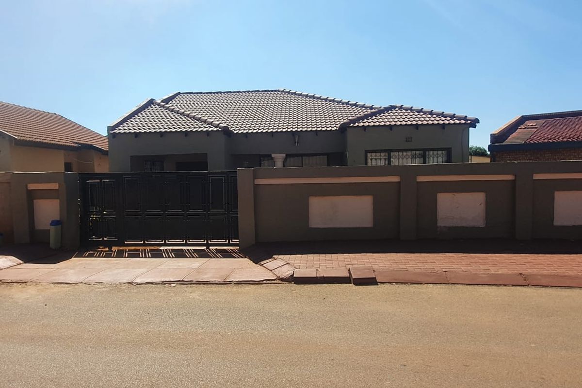 Front view of a single-story house featuring a tiled roof, secure perimeter wall with a metal gate, and paved street-side access.