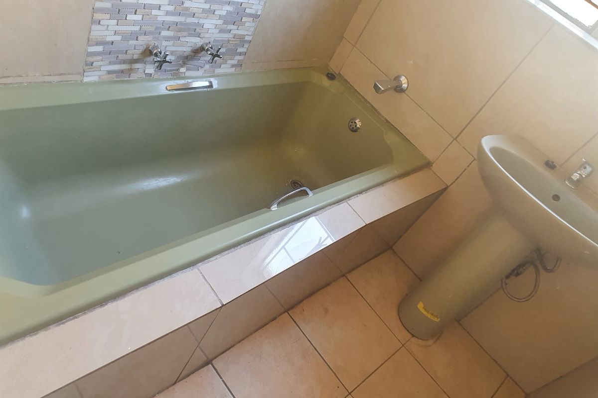 A functional bathroom featuring a built-in bathtub with mosaic tile splashback and a pedestal basin, finished with neutral ceramic floor tiles.