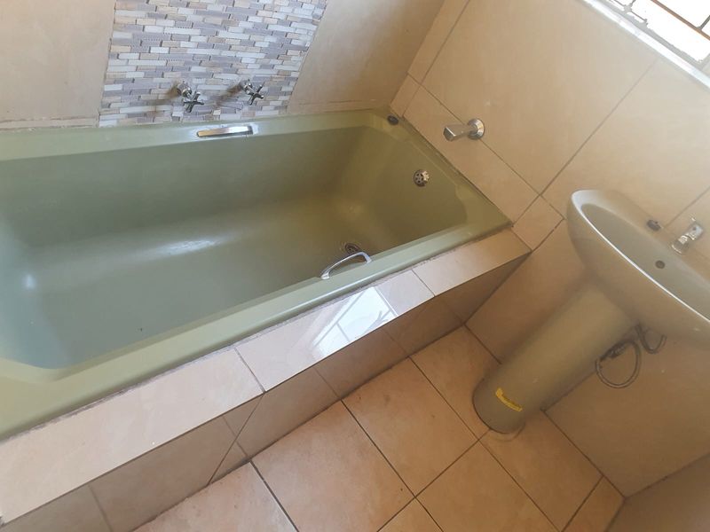A functional bathroom featuring a built-in bathtub with mosaic tile splashback and a pedestal basin, finished with neutral ceramic floor tiles.
