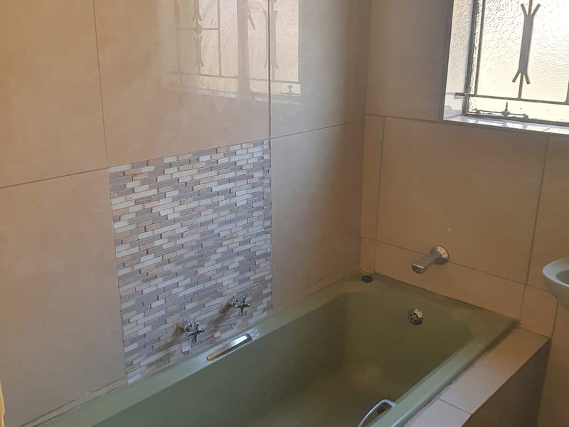 A bathroom featuring a built-in bathtub with tiled surround, mosaic accent detailing, and a window with security bars.