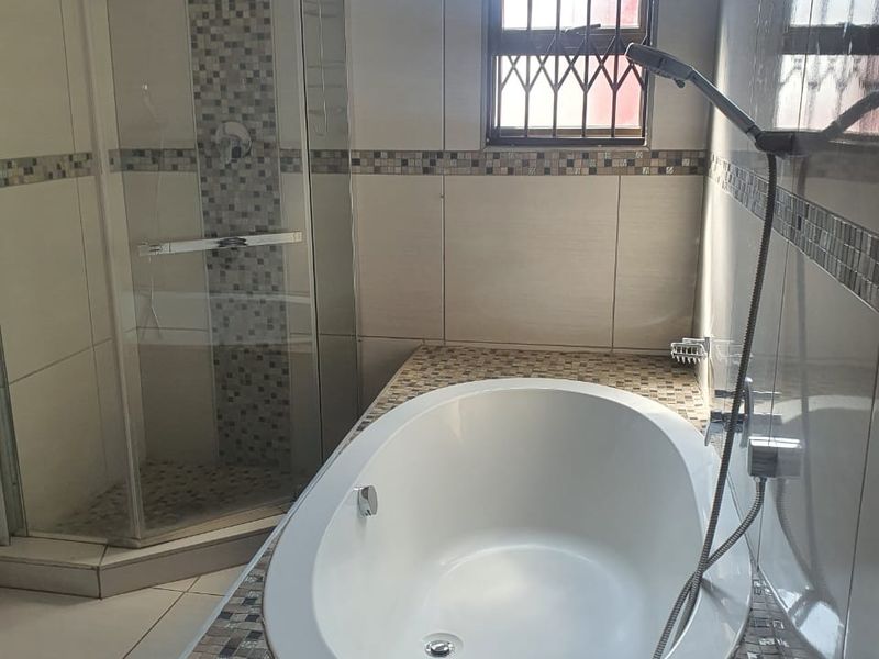 A clean, modern bathroom featuring a built-in oval bathtub, a separate glass-enclosed shower, and decorative mosaic tile detailing.