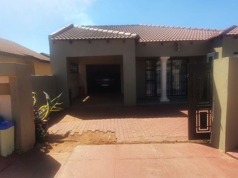 Front elevation of a house featuring a tiled roof, covered carport, paved driveway, and secure gated entrance.