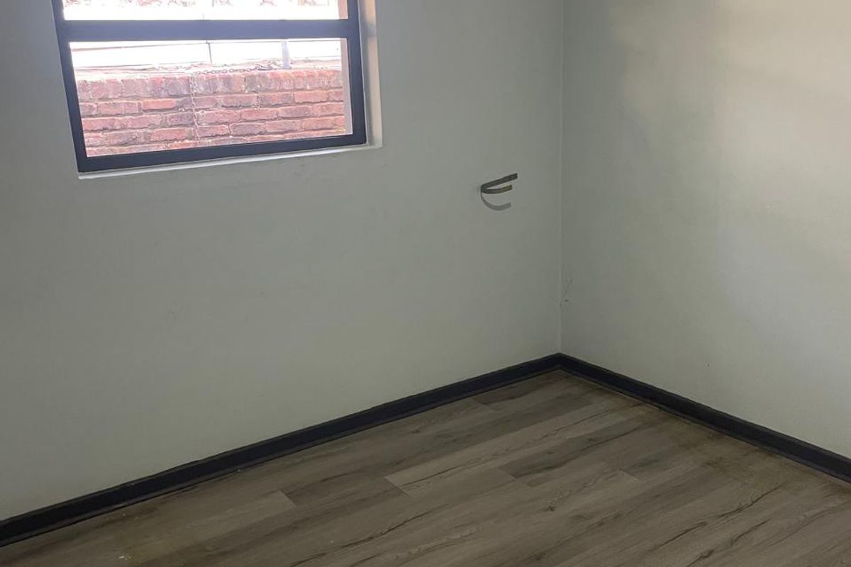 An empty bedroom featuring modern laminate flooring, a metal-framed window, and exposed electrical wiring, offering a blank canvas for personalization.