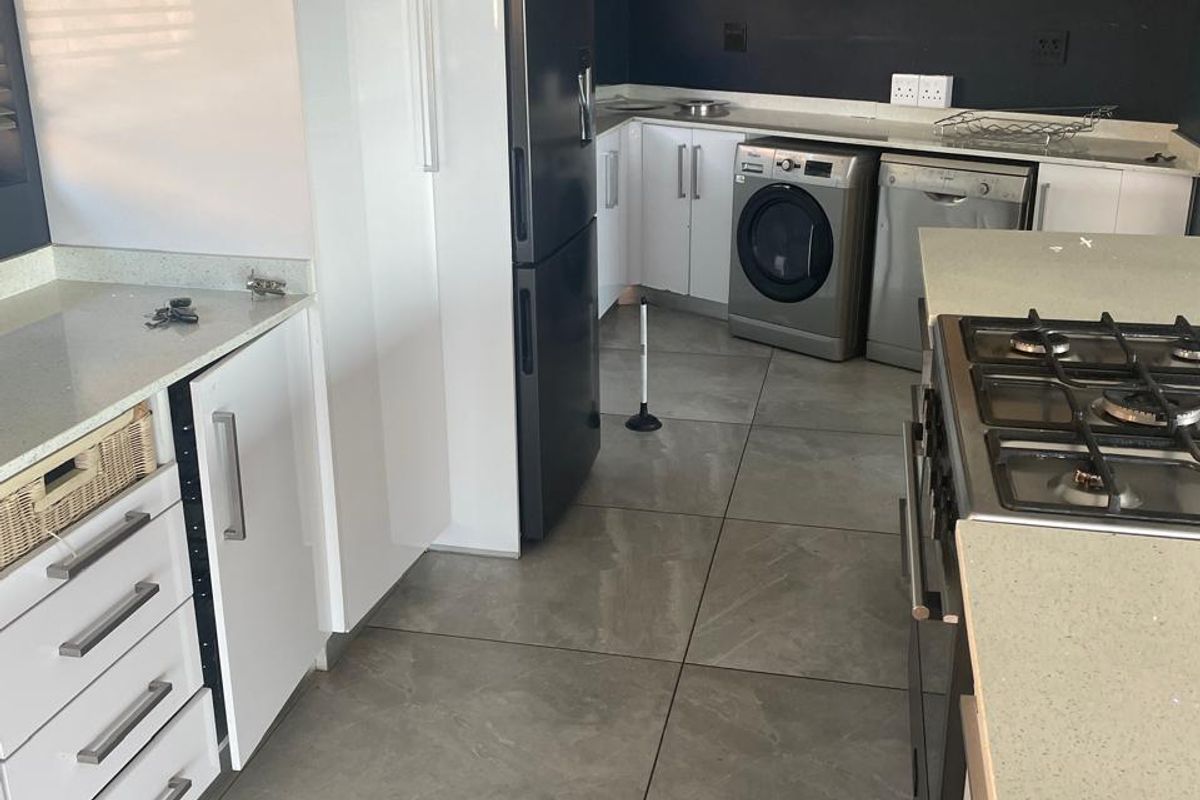 Modern kitchen featuring stone countertops, gas hob, built-in oven, and ample fitted cabinetry with large format floor tiles.