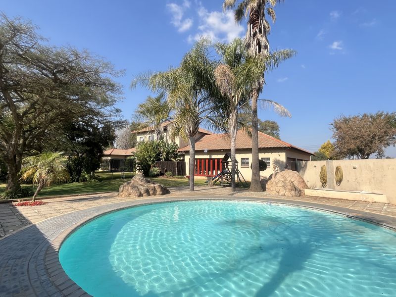 A spacious outdoor pool area featuring a circular swimming pool, paved surround, and established garden with mature trees and boundary walling.